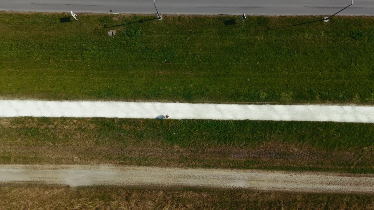 top down drone view of lone pedestrian walks along bright gravel trail in Zagreb's riverbank fields