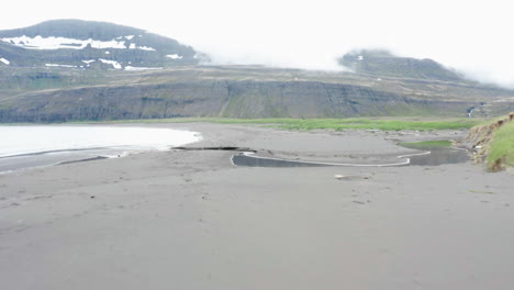 Low-flight-over-nordic-dark-sand-beach-in-Hornvik-bay,-Hornstrandir