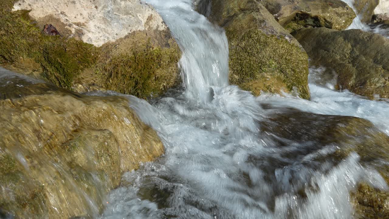 Acqua limpida scorre su rocce muschiose al rallentatore, mettendo in mostra le texture naturali