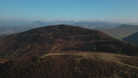 Hiker-walking-on-mountain-with-town-of-Keswick-and-misty-mountains-on-horizon-in-English-Lake-District-UK