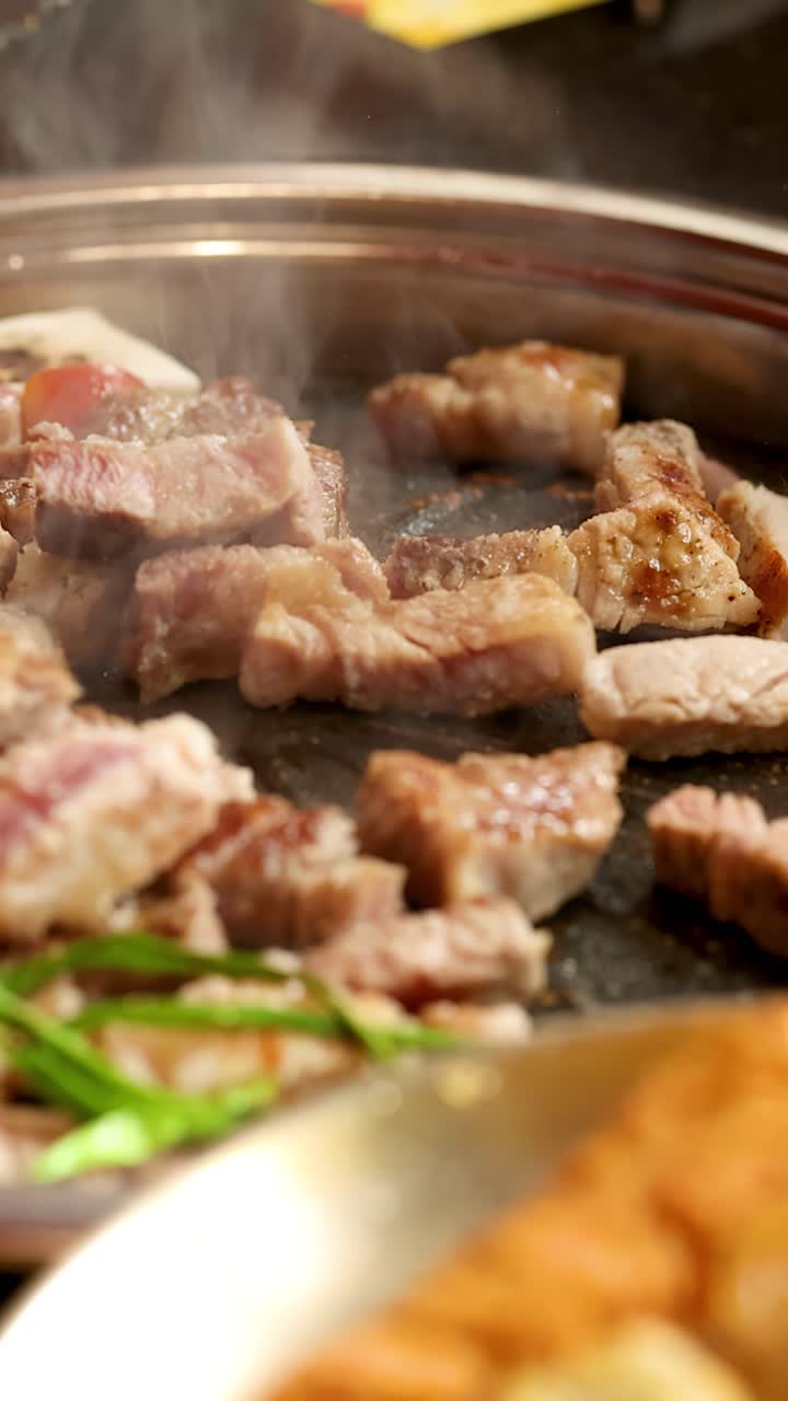 Gros plan sur de la poitrine de porc juteuse grillant sur un barbecue de table, avec de la vapeur qui s'élève et un éclairage doré.