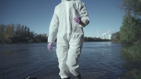 suitcase with test tubes and person in protective suit checking river sample, outside view, industrial background