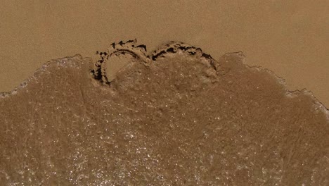 Close-up-of-a-heart-sign-in-the-sand-that-is-washed-away-by-the-sea