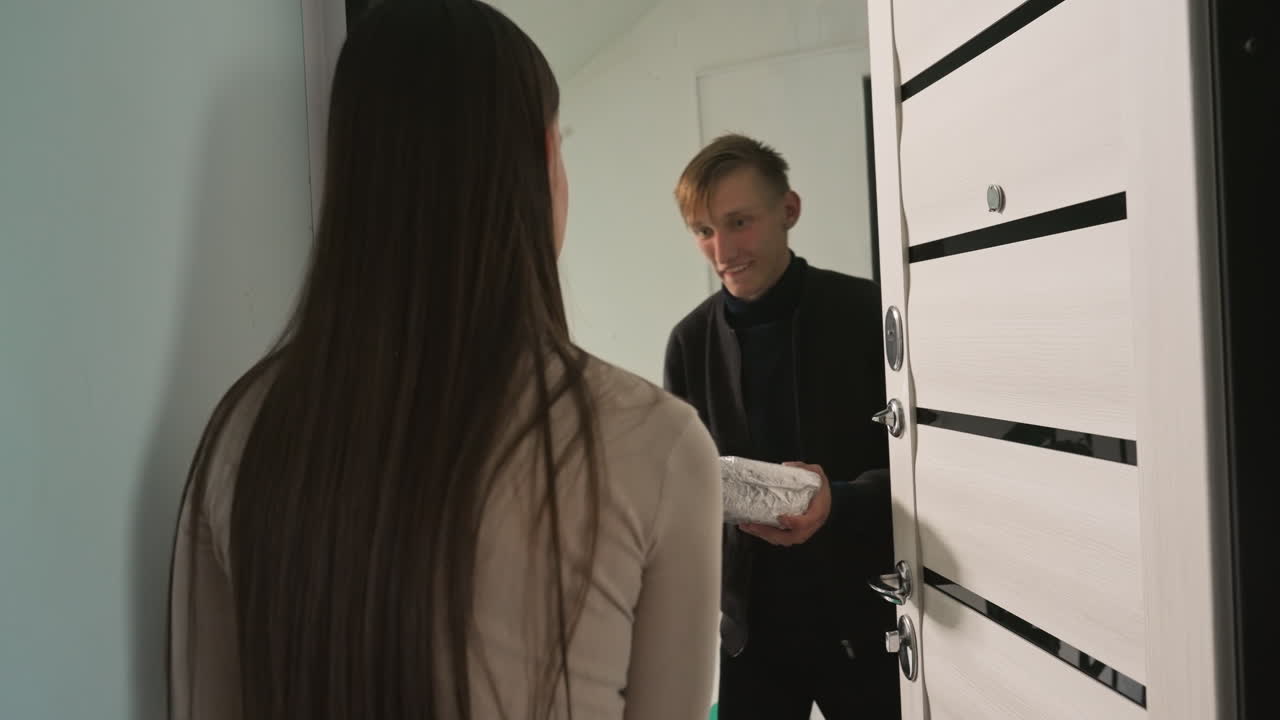 caucasian woman receives bulky fitness package at apartment door, male courier presents dumbbell box for handover, recipient inspects packaging and signs receipt, cordial exchange in bright hallway