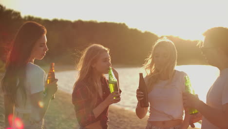 girls celebrate a birthday on the open air party with friends with beer and good mood. they dance in the summer evening near the lake coast. this is carefree party at sunset.