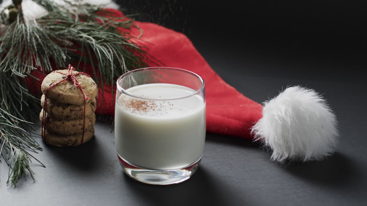 video de galletas de navidad, un vaso de milk, sombrero de santa claus y espacio de copia en fondo negro