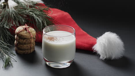 Vídeo-De-Galletas-Navideñas,-Vaso-De-Leche,-Sombrero-De-Santa-Claus-Y-Espacio-Para-Copiar-Sobre-Fondo-Negro