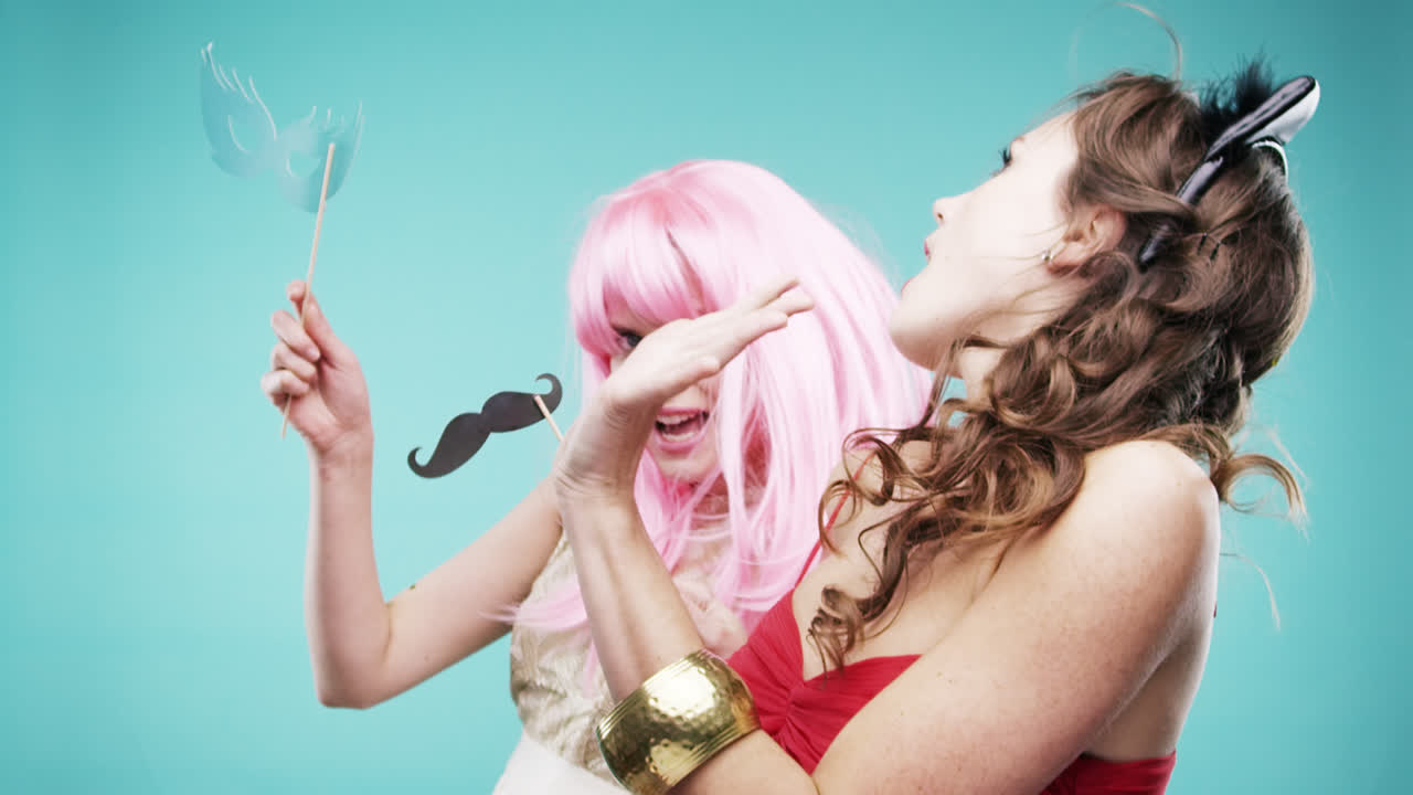 빨간 드레스와 분홍색 머리카락을 입은 여자 친구들이 느린 움직임의 파티 사진 부스에서 춤추고 있습니다.