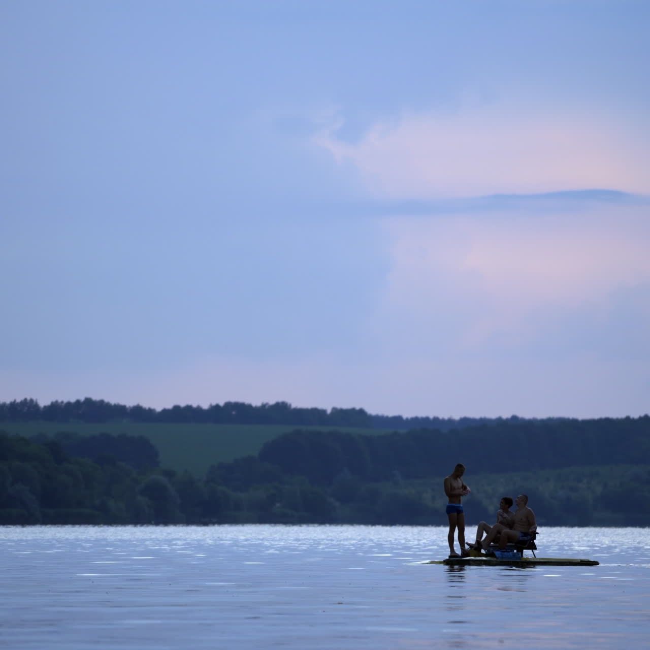 Three men sailing in a catamaran on the river in summer. Guys in swimming trunks only, floating in a pedal boat on a beautiful natural background in the evening.