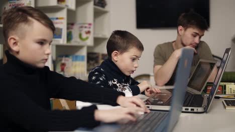 Dos-Niños-Pequeños-Escribiendo-Algo-En-Los-Teclados-De-Una-Computadora-Portátil-Mientras-Su-Maestro-Programador-Está-Sentado-Cerca.