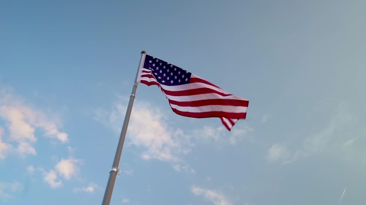 Bandiera americana che sventola al vento contro un bellissimo cielo blu con leggere nuvole bianche in lontananza