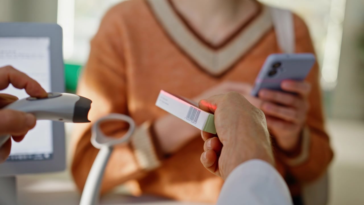 Primer plano de las manos de un farmacéutico escaneando medicamentos mientras un cliente desconocido los toma en el interior.