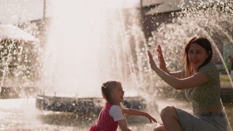 laughing girl splashes water on mother near fountain jets