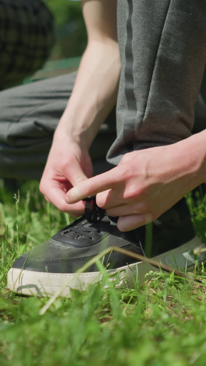 Close-up of three people on a grassy field, two of them squatting to adjust their shoelaces while a young child stands nearby