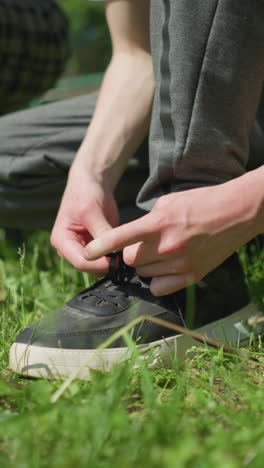 close-up of three people on a grassy field, two of them squatting to adjust their shoelaces while a young child stands nearby