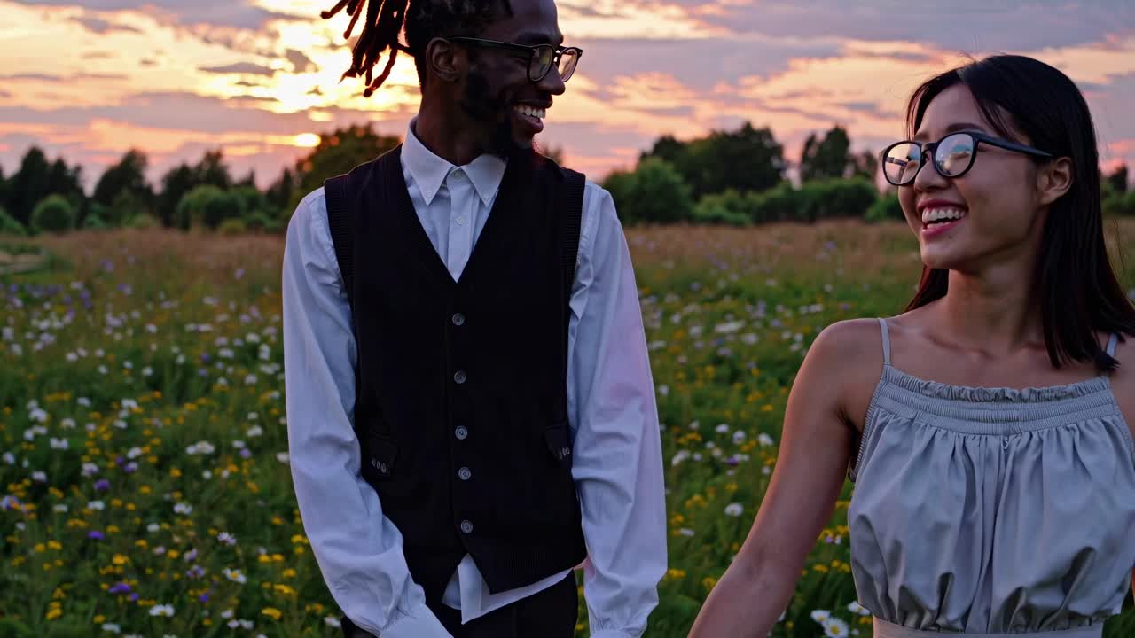 A joyful couple walks through a wildflower field at sunset, captured in a candid, eye-level video