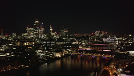 Night-scene-of-large-town.-Modern-tall-buildings-on-City-financial-and-economical-centre.-Backwards-reveal-of-Thames-river-and-its-bridges.-London,-UK