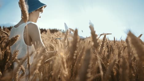 cinematic boy in a hat playing with airplane in the golden wheat field, moving camera, steadicam shot