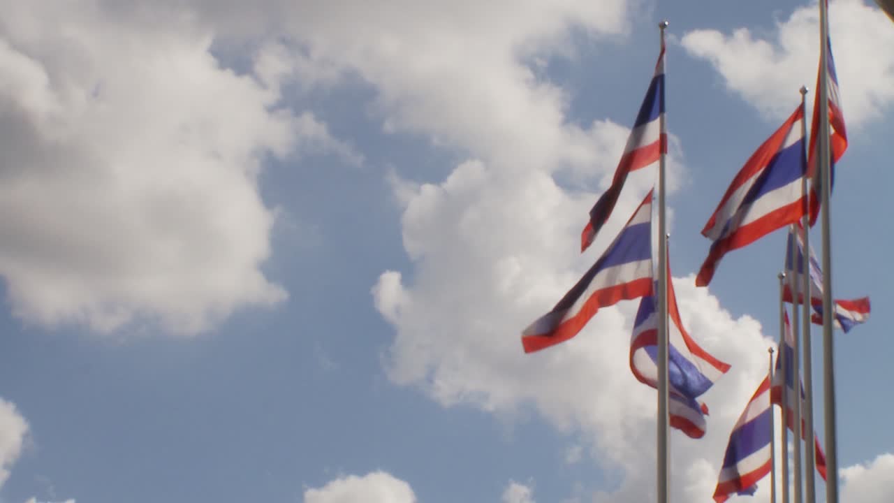 Left framed Thai flags on poles against white clouds in a blue sky