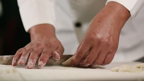 rolling the round edge of a dumpling with a wooden pin - side view chef in traditional uniform