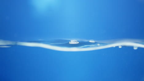 Waves-of-crystal-clear-blue-mineral-water,-creating-some-tiny-bubbles-and-droplets-of-in-a-water-tank