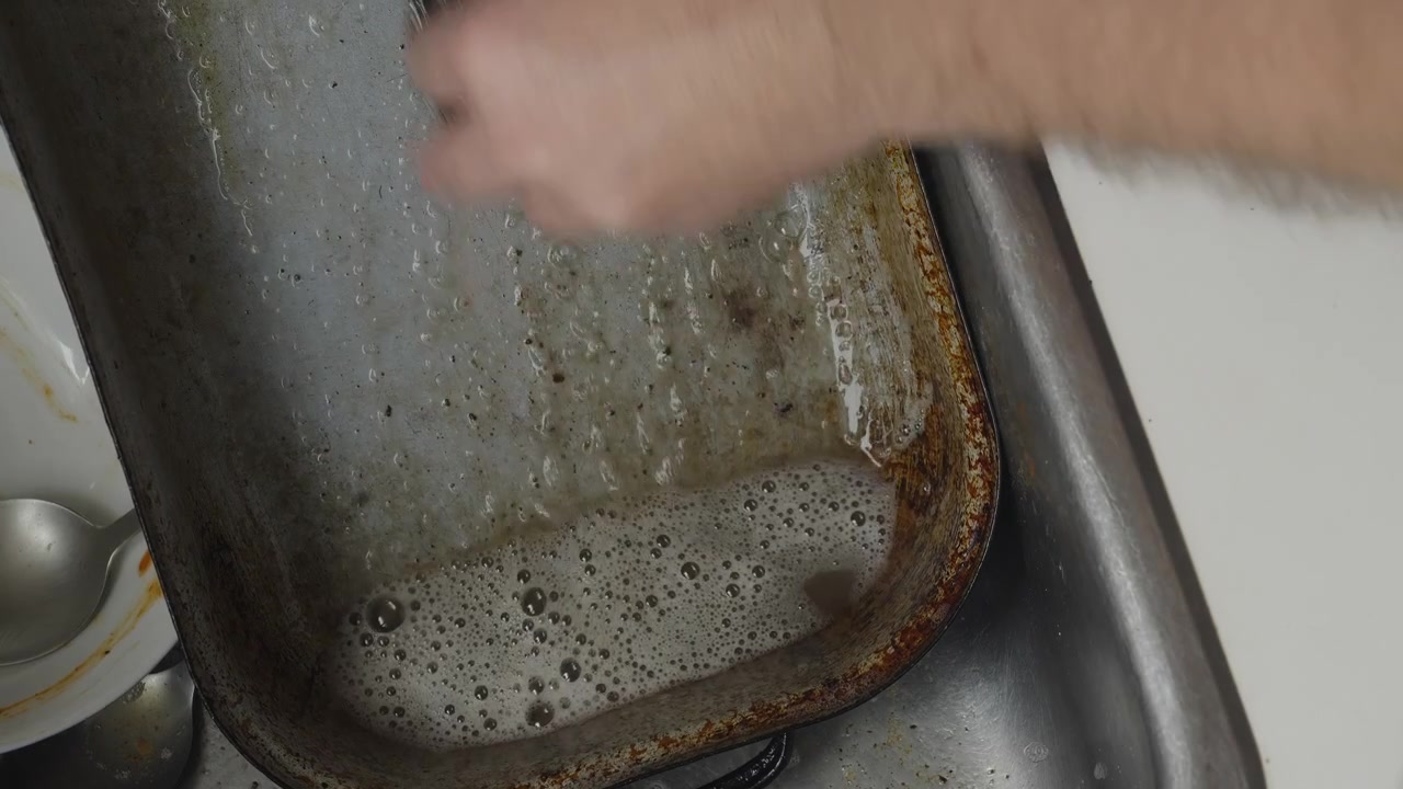 Et fugleperspektiv fanger intensiv rengøring, når fastbrændte madrester fjernes fra en ovnpande. Ideel til temaer om rengøring, hygiejne, huslige pligter og vedligeholdelse af hjemmet.