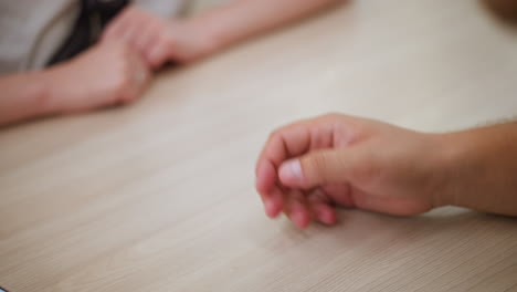 primer plano de una pareja que se toman de la mano afectuosamente, mostrando sus anillos como símbolo de conexión y amor, mientras las manos se encuentran tiernamente en la superficie lisa de la mesa de madera