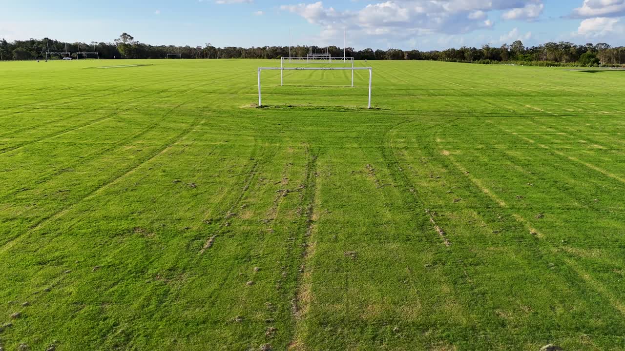Vista aérea de um campo de futebol com balizas, capturada por um drone sob céu limpo, exibindo grama verde exuberante