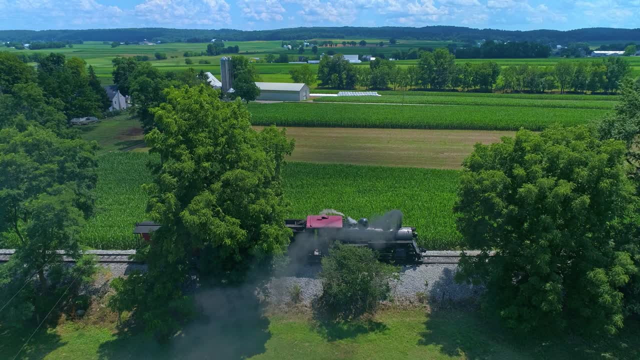 푸른 농지를 가로질러 증기를 뿜어내는 고풍스러운 증기 엔진과 카부스의 공중 전망