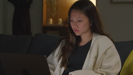 woman spending evening at home sitting on sofa with laptop computer looking at social media streaming or scrolling online 1