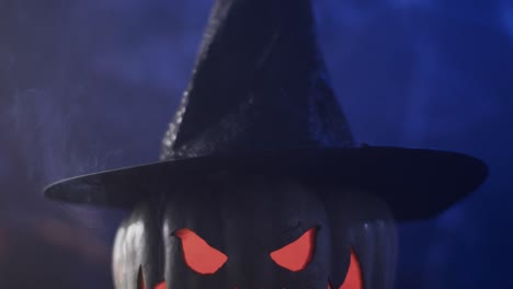 video of halloween carved pumpkin in hat and smoke with copy space on blue background