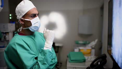 cirujano masculino biracial mirando con escáneres de rayos x en la sala de operaciones en el hospital, cámara lenta