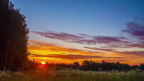 Timelapse-of-sunrise-across-fiery-sky-over-meadow-near-forest