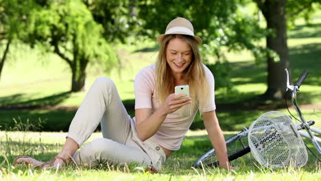 Pretty-girl-using-smartphone-beside-her-bike-in-the-park