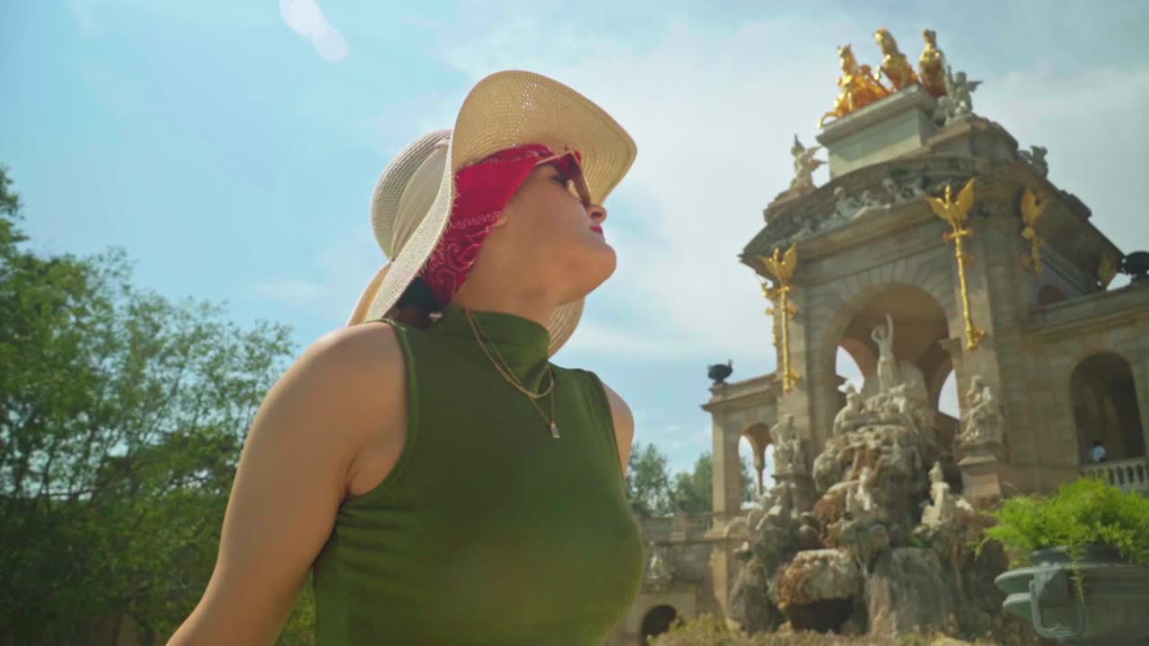 Stunning footage of a young caucasian girl in a green dress and hat joyfully posing in front of Cascada Monumental - Gaud&iacute;'s fountain in Parc de la Ciutadella