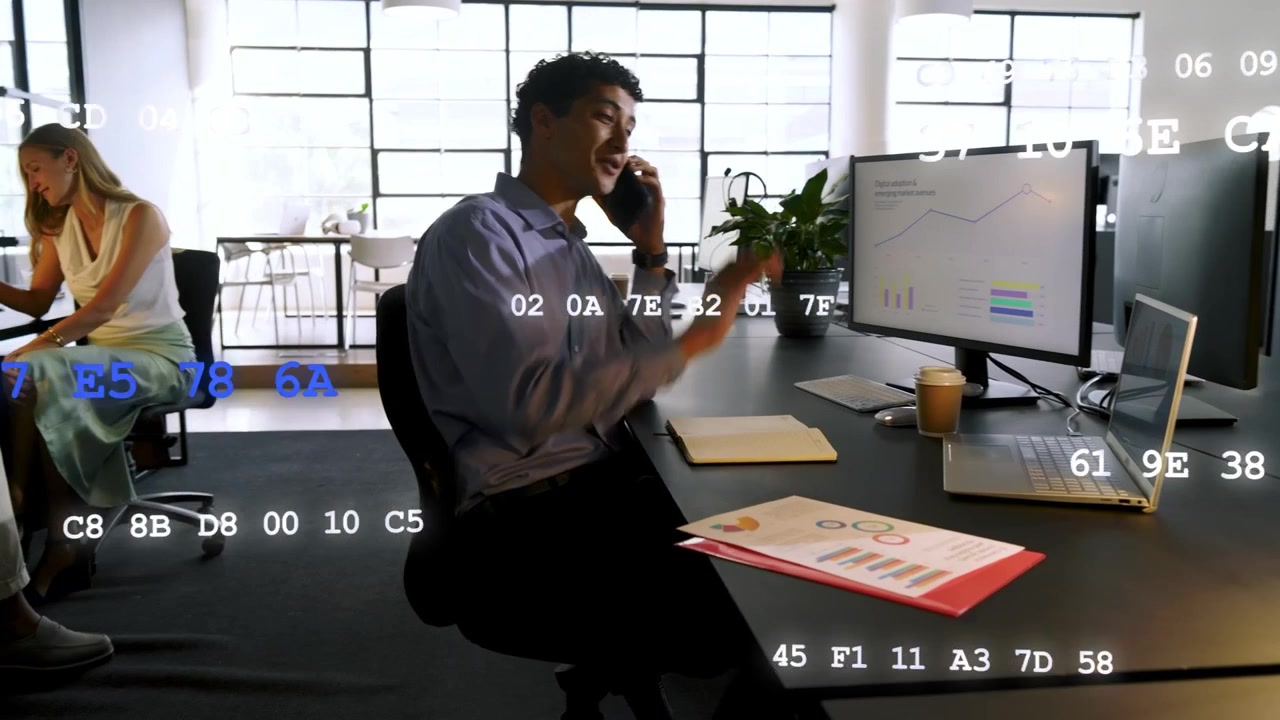 Seated analyst answering call and noting in office, codes scrolling over charts for finance update