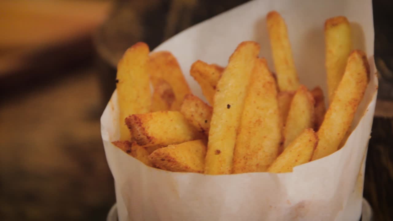 Homemade, crispy and delicious rustic french fries displayed in a metal cup with paper wrap - slider motion, close up