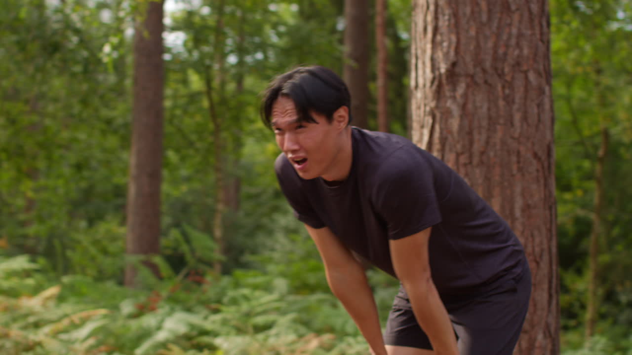 피곤한 중성인 남자가 야외에서 운동을 하고 숲을 가로질러 달리고 숨을 쉬기 위해 멈추고 실시간으로 습니다.