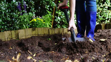 person mixing soil with shovel in garden