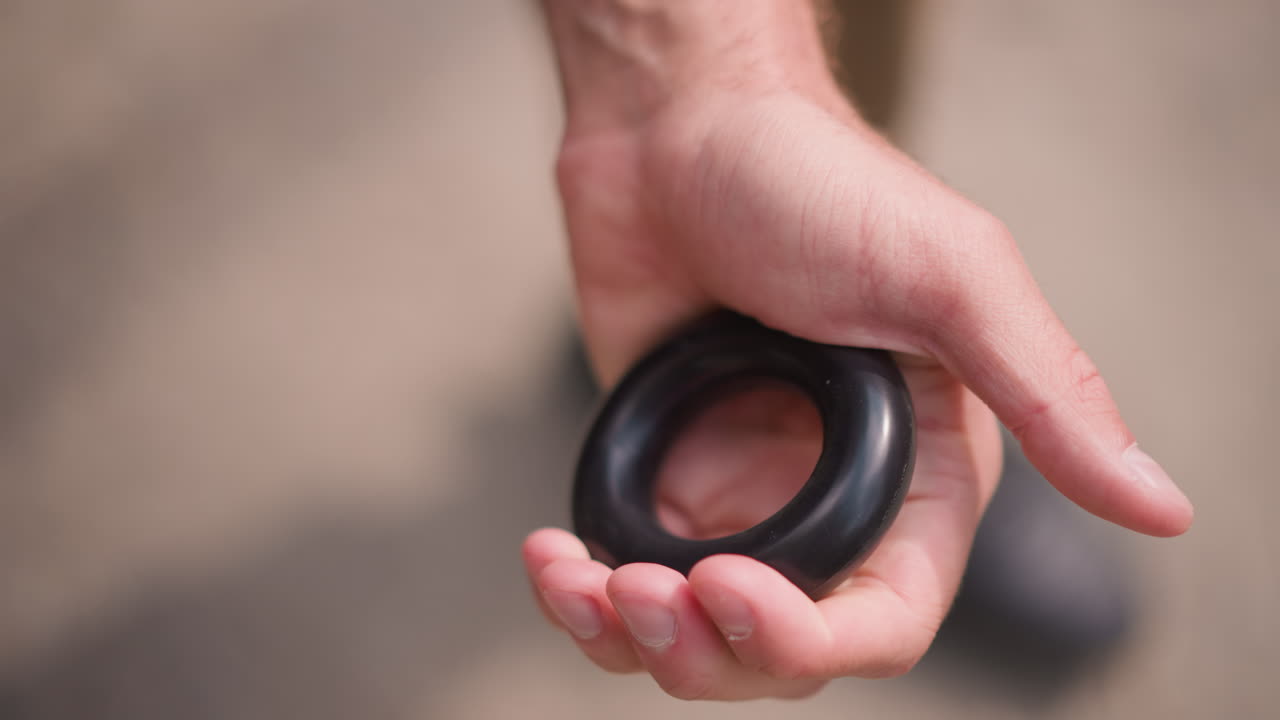 White Man Kneeling Squeezing Black Hand Ring With Force, Close Detail On Curled Fingers And Palm Pressure, Gritty Outdoor Surface, Concentrated Training For Grip And Forearm Power