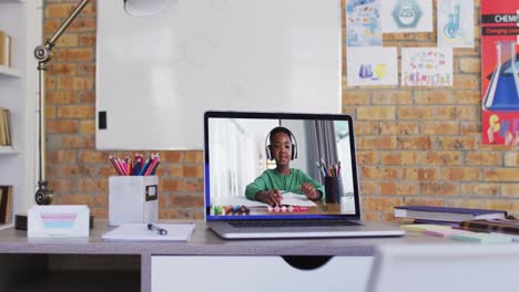 webcam view of african american boy doing homework on video call on laptop on table at school