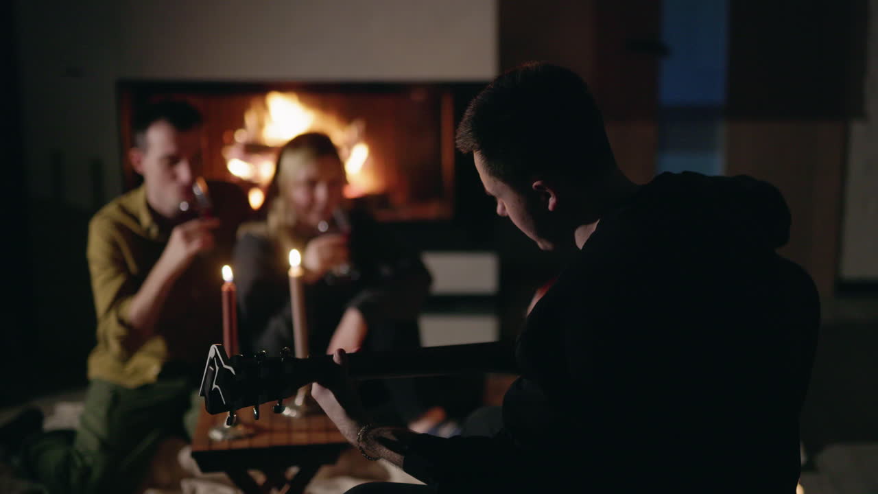amigos se reúnen alrededor de la chimenea tocando la guitarra.