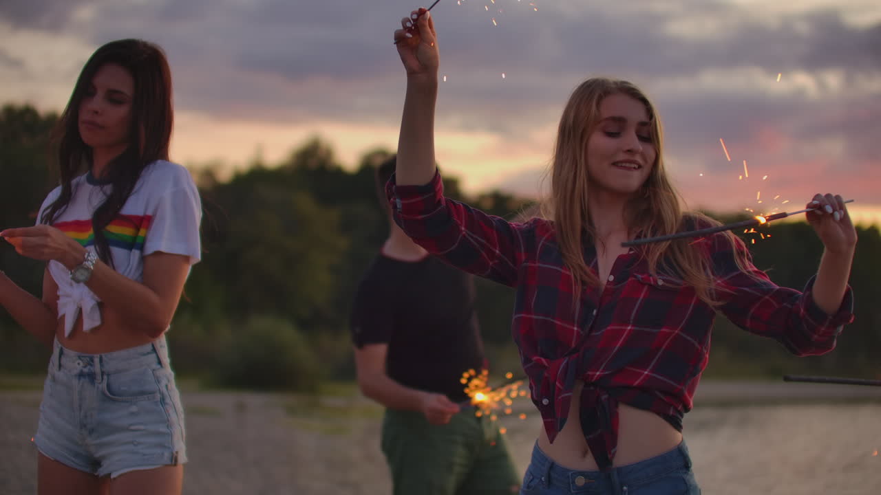 los adolescentes están bailando con grandes luces bengalíes en la costa de arena. esta es una loca noche de verano en la fiesta al aire libre.