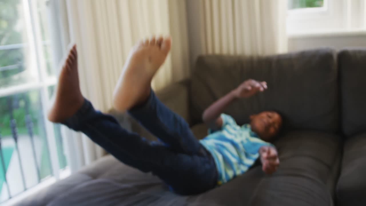 Smiling african american boy jumping on the couch at home