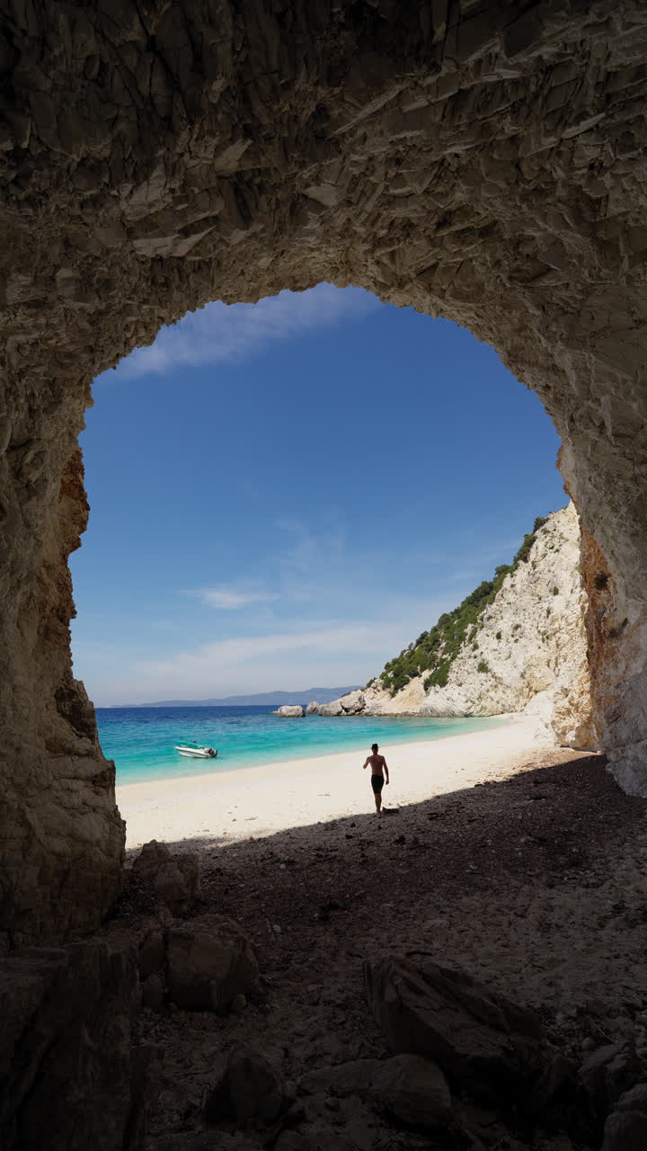 Man walking out from sea cave opening toward Platis Ammos Beach on Ithaca Island, Greece, Vertical