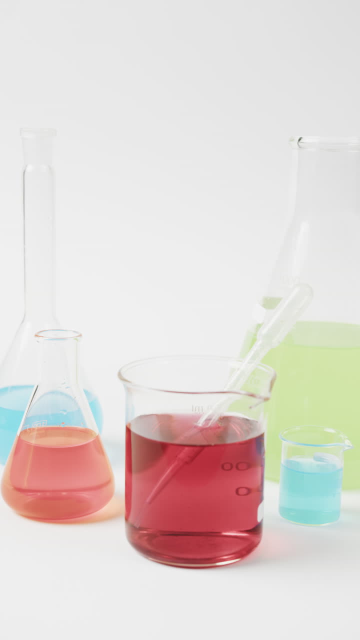 Vertical video of coloured liquids in flasks on white background