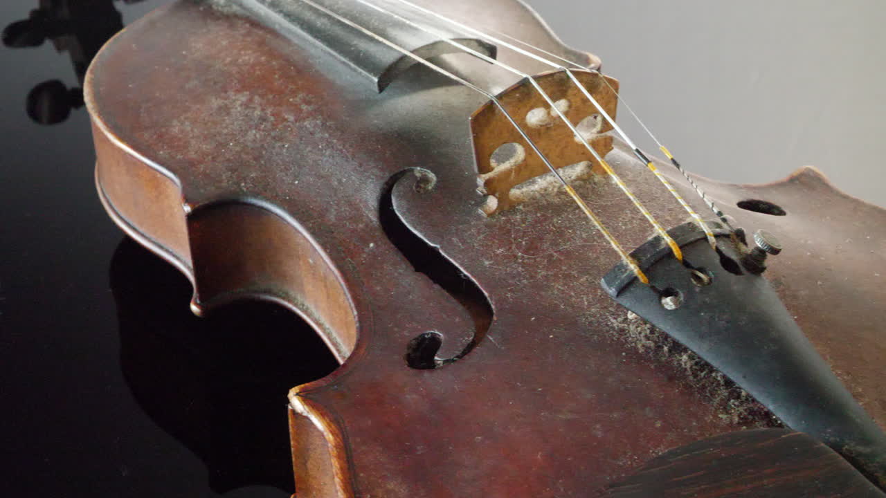 교향악단의 반짝이는 검은색 그랜드 피아노에 놓인 더러운 오래된 빈티지 바이올린 악기