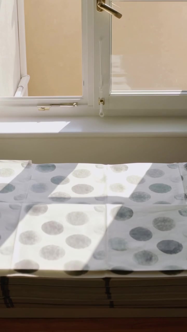 Vertical video: Lifting polka-dot fabric revealing white window shadow on sill, with brass handle