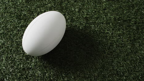 White-rugby-ball-on-sunlit-grass-with-copy-space,-slow-motion