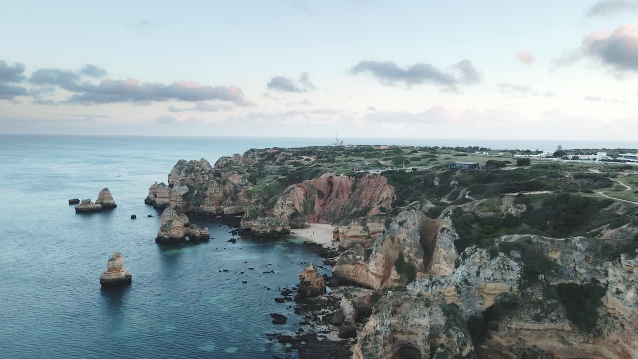 Aerial drone glides forward above rugged limestone cliffs and a secluded sandy bay in Lagos, Portugal